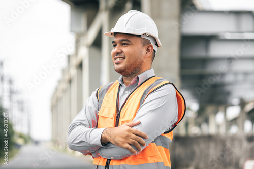 Asian engineer handsome man or architect looking construction with white safety helmet in construction site. Standing at highway concrete road site.