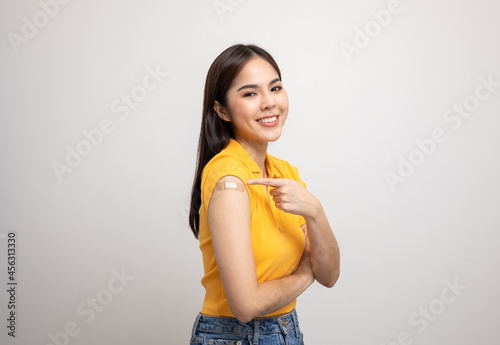 Vaccination. Young beautiful asian woman in yellow shirt getting a vaccine protection the coronavirus. Smiling happy female showing arm with bandage after receiving vaccination. photo