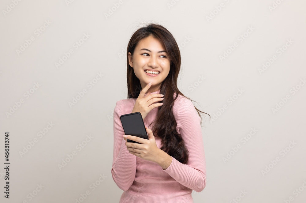 Pretty young asian woman using smartphone standing on isolated white background feeling happy. Shopping online payment with mobile phone. Excited and surprised female holding cellphone. Pretty young asian woman using smartphone standing on isolated white background feeling happy. Shopping online payment with mobile phone. Excited and surprised female holding cellphone.