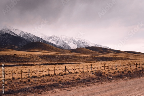 Dry grassland with rolling hills by the snowy Andes mountains in Valle de Uco  Mendoza  Argentina  in a dark cloudy day.