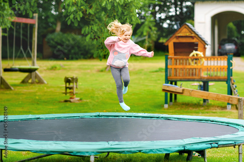 Little preschool girl jumping on trampoline. Happy funny toddler child having fun with outdoor activity in summer. Sports and exercises for children.