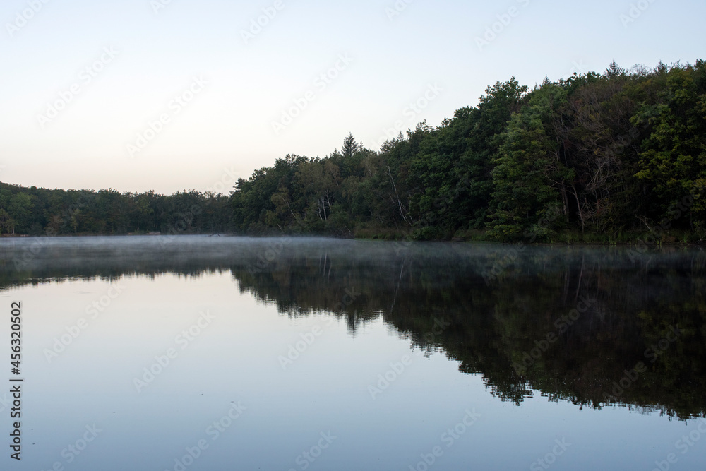 reflection of a forest by the lake with morning mist