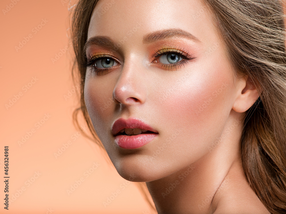 Fototapeta premium Portrait of a beautiful woman with a long blond hair. Model with beautiful hairstyle - isolated on beige background. Beige eye makeup with a long false black eyelashes.