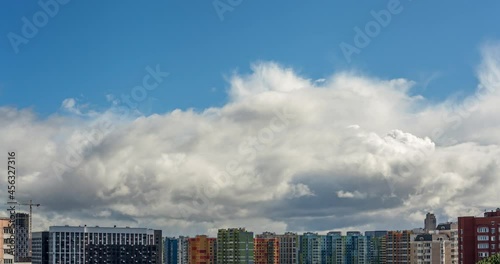 Timelapse of clouds rapidly running across blue sky over modern city district at daytime. Colorful buildings illuminated by the sun. Cinematic skyline time lapse. 