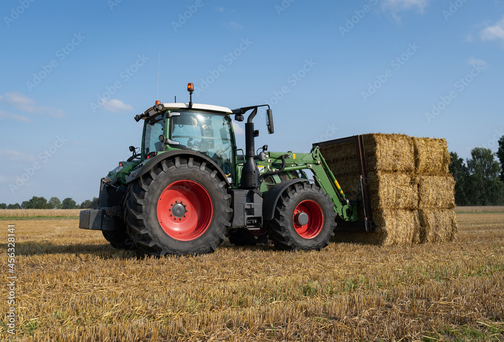 Strohernte - Traktor mit Frontlader beim Beladen eines Transportanhängers mit Strohballen. Strohernte - Traktor mit Frontlader beim Beladen eines Transportanhängers mit Strohballen.