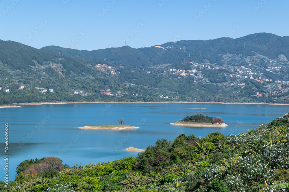 The shore of the lake is green, there are some small islands in the center, and the sky and water are blue