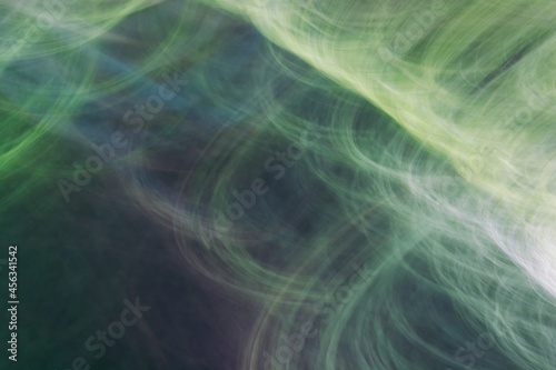 Drawing with light, depicting rays, circles, thin lines, glare. Abstract background in shades of green.