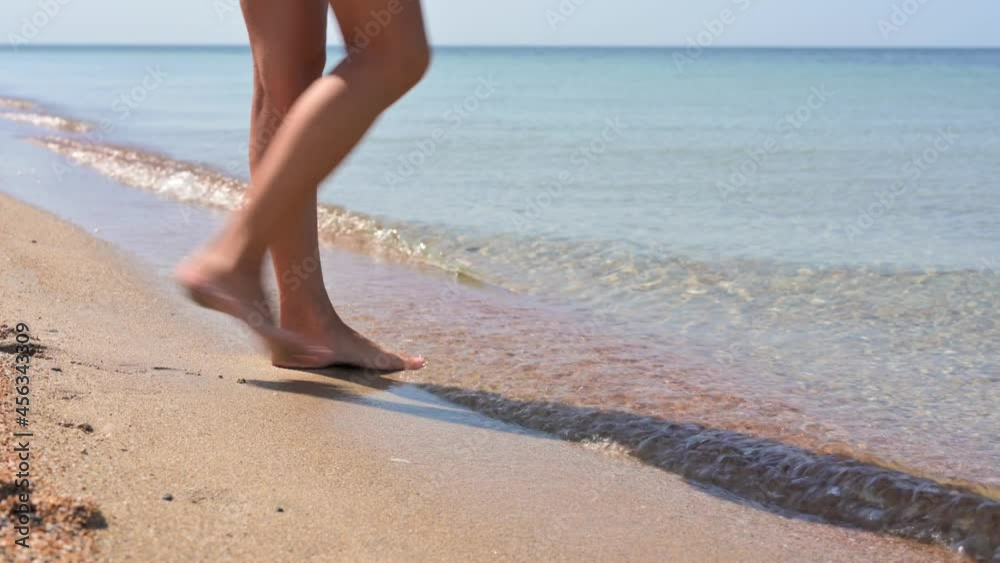 Female feet on the seashore close-up. The girl comes up to the sea and touches the water with her foot. Selective focus on the leg. Female feet on the seashore close-up. The girl comes up to the sea and touches the water with her foot. Selective focus on the leg.