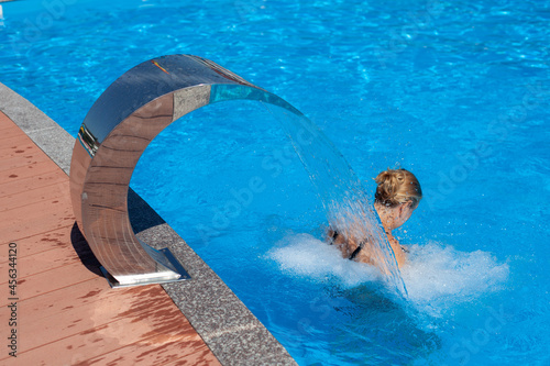 Woman is resting at tropical resort. Relaxation and hydro massage treatment under tropical waterfall in spa center on shore of seaside resort in summer. 