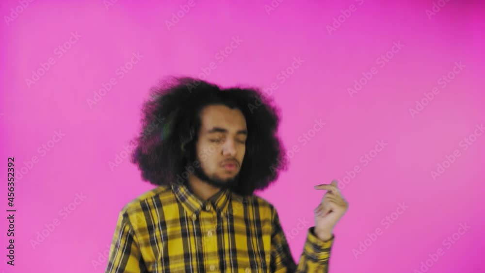 A young man with an African hairstyle on a pink background is dancing. Dancing on a colored background.