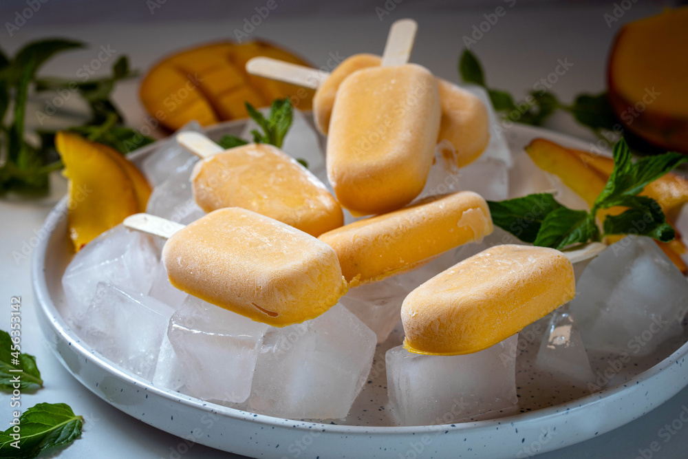Ice cream sorbet from mango and banana. Ice cream on a stick in a large plate with ice cubes, garnished with mint and mango. Ice cream sorbet from mango and banana. Ice cream on a stick in a large plate with ice cubes, garnished with mint and mango.