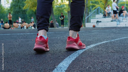 Guy in sport uniform warms up before playing on street basketball court. Sportsman hits ball on asphalt. Boy does exercises before competition. Basketballer training. Baller, player practises drills photo