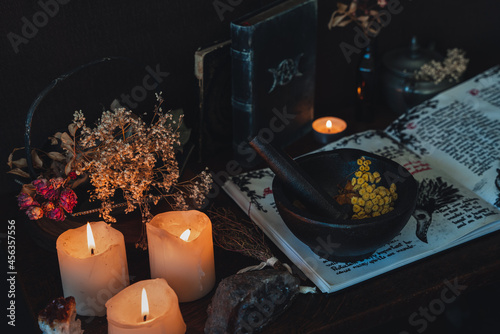 Wiccan witch altar prepared for casting a spell with an open Book of Shadows and pestle and mortar. Old spell books, crystals, burning lit candles, dried flowers in dark night background