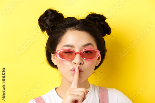 Summer fashion concept. Close-up portrait of glamour asian woman in sunglasses telling a secret, asking be quiet, making hush taboo sign and winking at camera photo