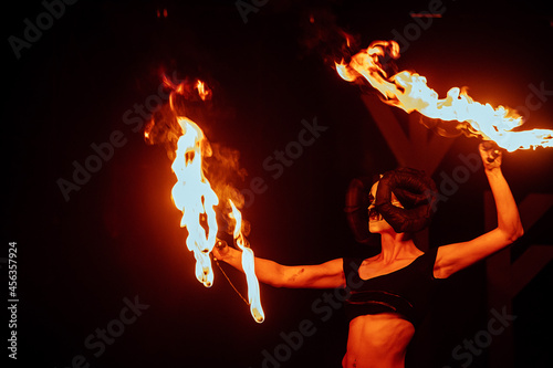 a fireshow artist in a mask of a mythical creature performs with fire. street culture festival. colorful mystical fire show at night
