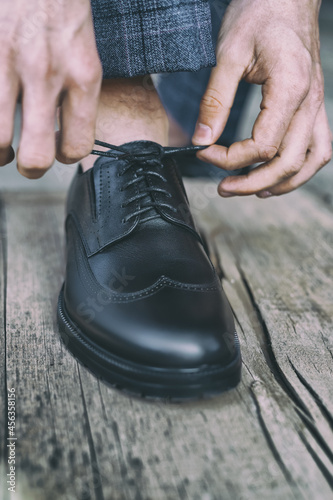 man ties his shoelaces on black patent leather shoes on old wooden floor, toned image