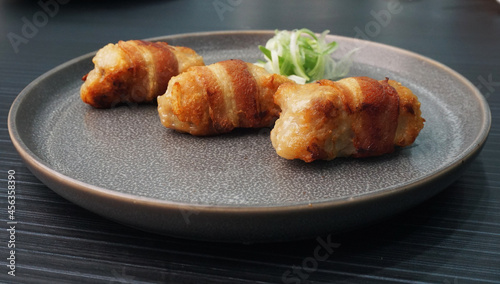 deep fried pork meatball wrapped with bacon roll in plate on dark grey wood table asian dim sum halal food restaurant cuisine banquet menu for cafe