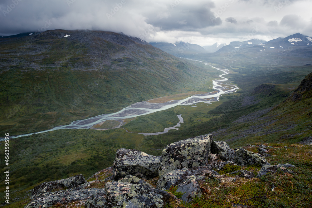 Wild river winds through remote arctic valley on a cloudy, rainy day of arctic summer. Rapa river in Sarek National Park, freedom. Epic, harsh arctic landscape.
