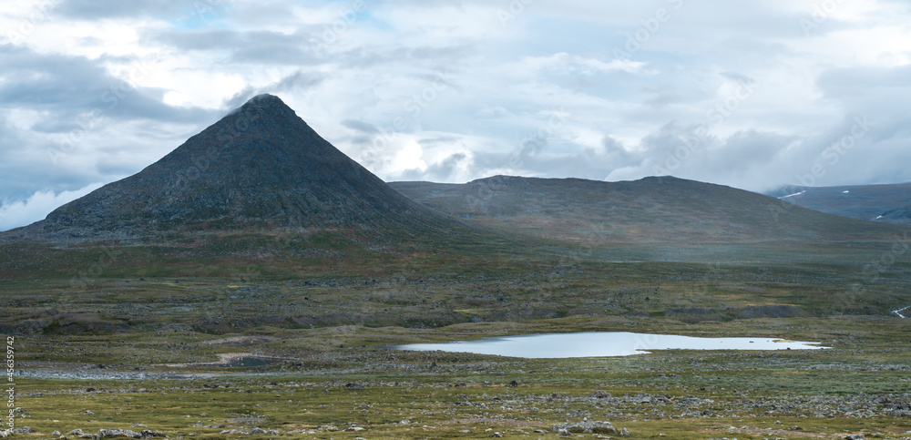 Pyramid shape of Mt Slugga in Swedish Lapland with lake in front viewed from Stora Sjofallet national park on a cloudy day of arctic summer.