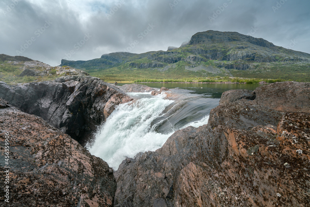 Closeup, wide, low angle shot of mighty Stuor Muorkkegarttje waterfall on Lulealven river on a partly cloudy day of arctic summer. Stora Sjofallet national park, Sweden.