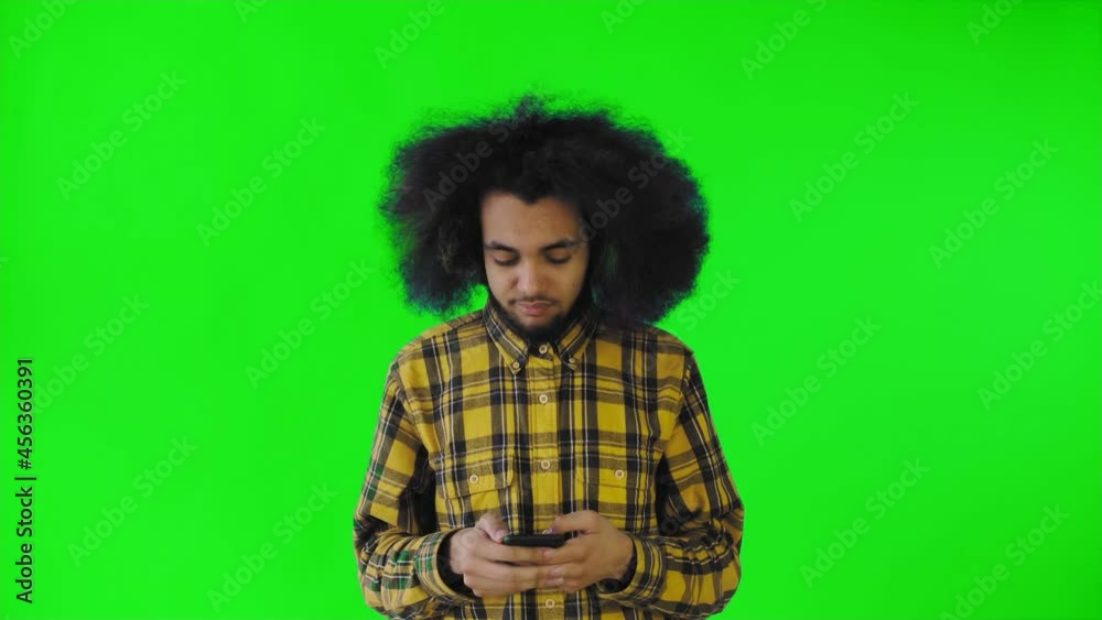 A young man with an African hairstyle on a green background is talking into his phone. A young man with an African hairstyle on a green background is talking into his phone.
