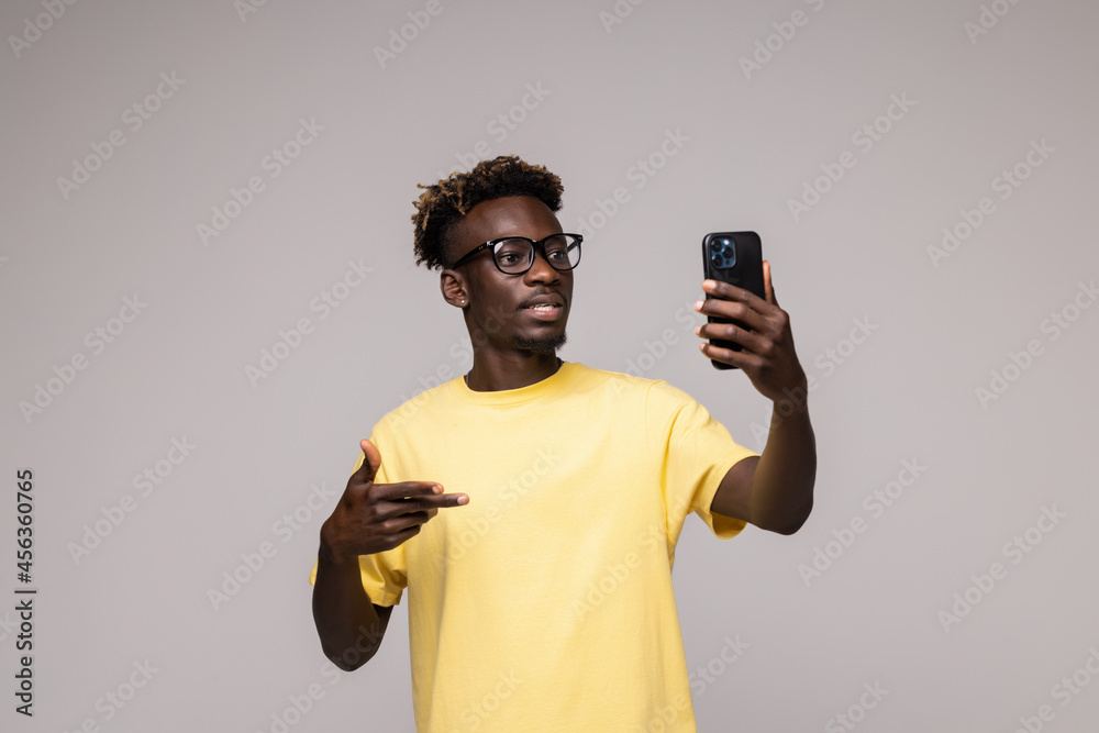 young afro man smiling happy taking selfie self portrait picture with mobile phone looking excited having fun posing cool isolated in grey background young afro man smiling happy taking selfie self portrait picture with mobile phone looking excited having fun posing cool isolated in grey background