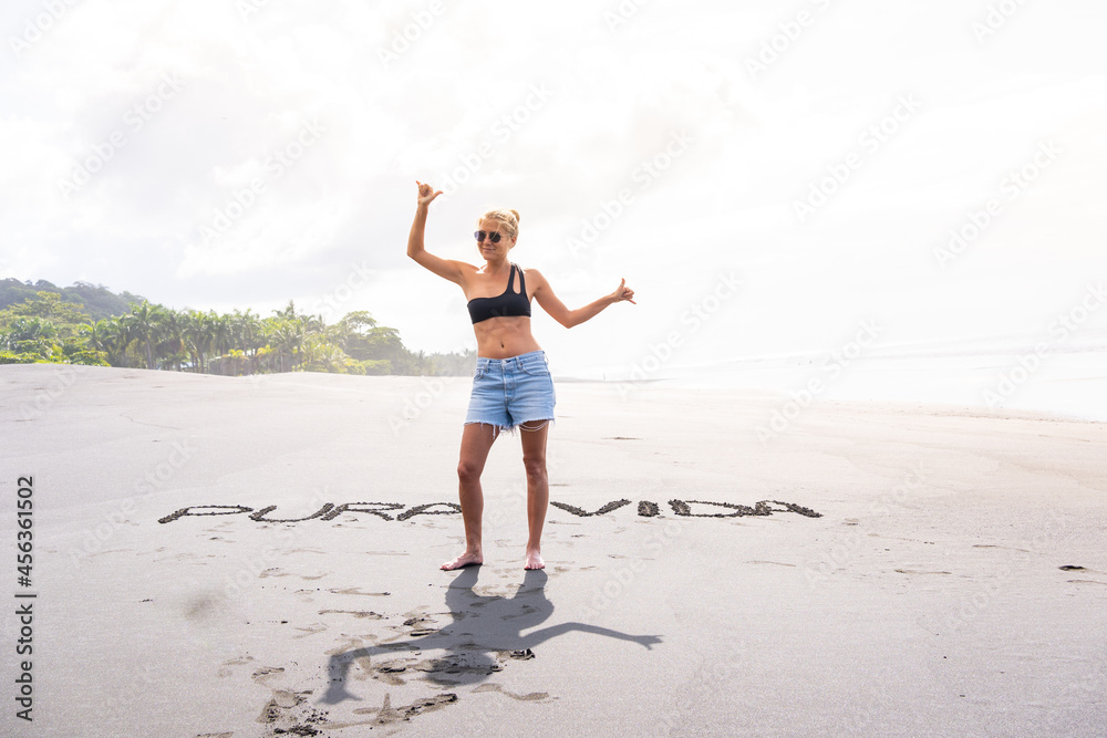 Woman standing on a beach with inscriptions in the sand gesturing to be happy