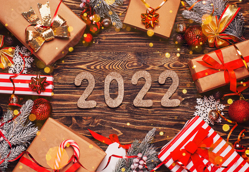 2022 new years golden numbers. Christmas background with gift boxes in craft paper with red ribbons, Christmas decorations, spruce twigs and snowflakes on rustic dark wooden background. 