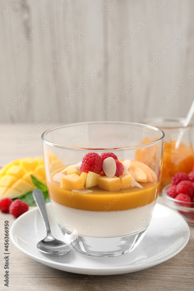 Delicious panna cotta with mango coulis, fresh fruit pieces and almond flakes on light wooden table Delicious panna cotta with mango coulis, fresh fruit pieces and almond flakes on light wooden table