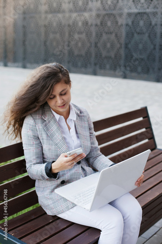 woman sitting on a bench working on laptop and mobile phone © Dina