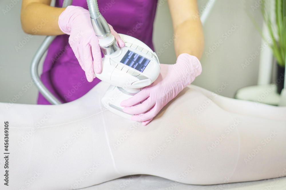 close-up of hand in pink gloves holding an LPG apparatus and giving lipomassage to woman's back and buttocks, in white slimming jumpsuit. Body aesthetic cosmetology. weight loss and LPG massage.