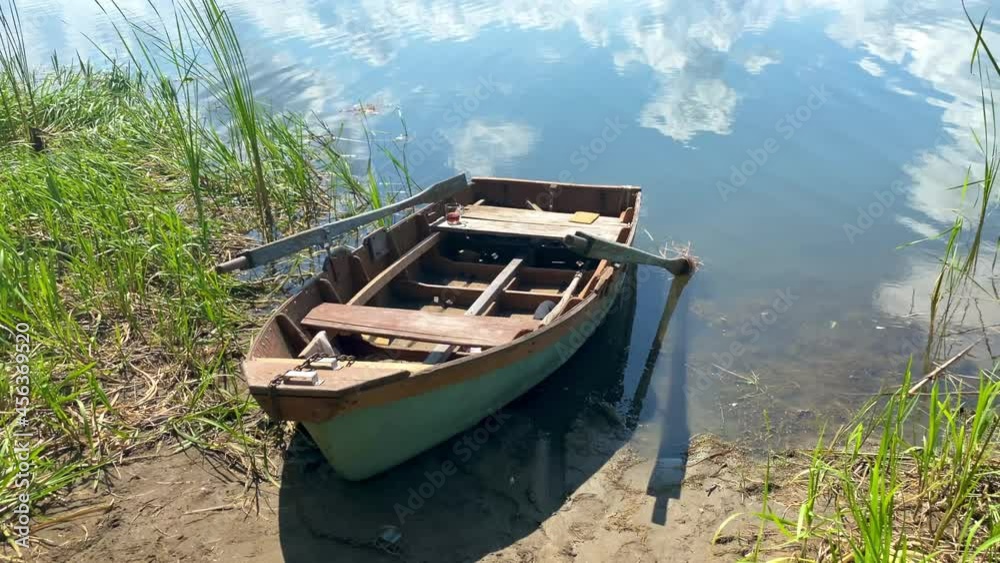 Wooden old fishing boat moored on the bank of the river in the reeds on a sunny day with blue sky and beautiful clouds. River landscape Wooden old fishing boat moored on the bank of the river in the reeds on a sunny day with blue sky and beautiful clouds. River landscape