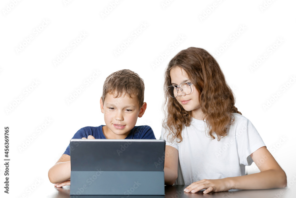 The interested brunettes boy and girl in glasses are sitting at the table by the tablet on isolated white background.  The concept of distance learning, interaction, communication.