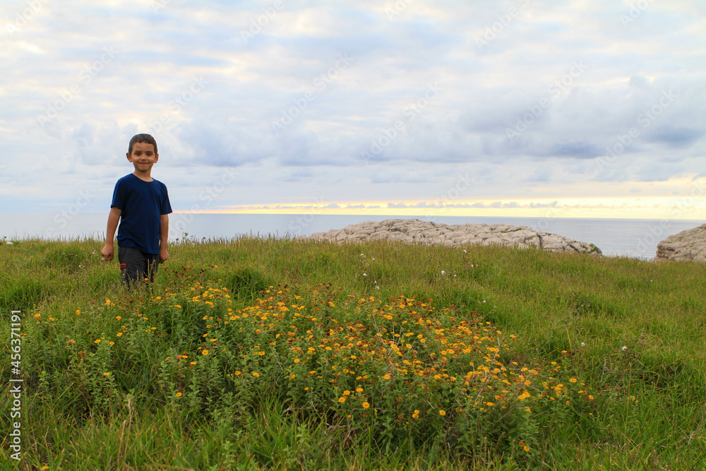 Niño jugando en el campo con el mar de fondo al atardecer