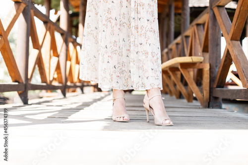 Women's beautiful legs in fashionable leather summer shoes with a heel in a fashionable skirt on a wooden walkway.