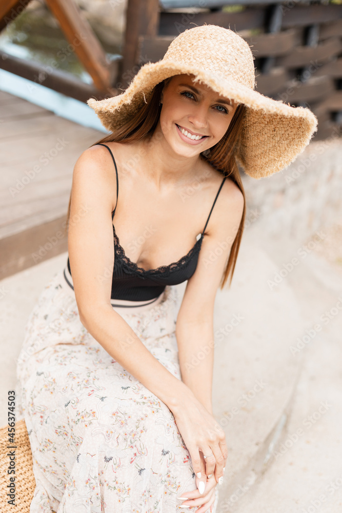 Happy fresh portrait of smiling pretty woman with straw hat in vintage lace lingerie sits and rest on the steps on a sunny day countryside