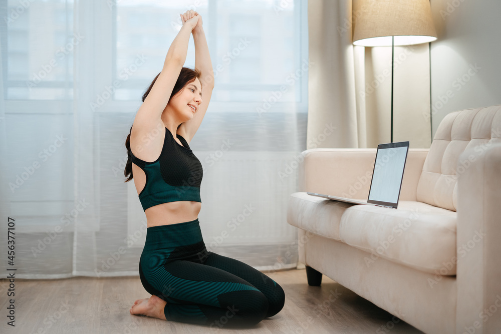 Fitness a woman in sports clothes does exercises looks at a laptop screen yoga lesson in the living room.Playing sports at home Fitness a woman in sports clothes does exercises looks at a laptop screen yoga lesson in the living room.Playing sports at home