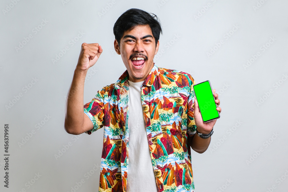 Asian man showing green screen of smartphone very happy pointing with hand and finger to the side