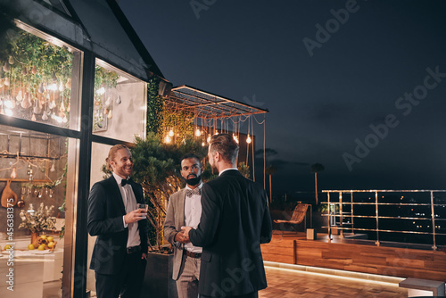 Three well dressed men drinking whiskey and communicating while spending time on party