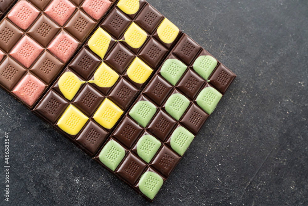 Multicolored fruit chocolate bars on black background. Handmade chocolate with mint, mango, orange, strawberry flavor. Healthy food concept, delicious chocolate sweets for kids, diet, sugar Multicolored fruit chocolate bars on black background. Handmade chocolate with mint, mango, orange, strawberry flavor. Healthy food concept, delicious chocolate sweets for kids, diet, sugar
