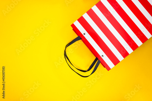 White and red striped paper shopping bag on yellow background. Black Friday sale shopping.