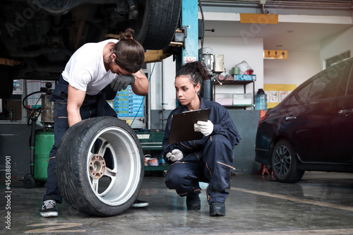 Two mechanic checking wheels at garage, car service technician man and woman checking and repairing the customer car at automobile service center, vehicle repair service shop concept.