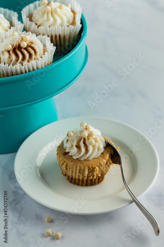 Mini pumpkin cheesecake on white plate with spoon, teal tray with more in background.