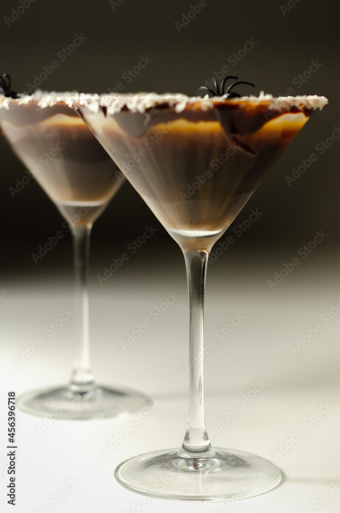 Alcoholic drink based on vodka and coffee liqueur served in a cocktail glass, decorated with chocolate, desiccated coconut and Halloween decoration in the shape of a spider Alcoholic drink based on vodka and coffee liqueur served in a cocktail glass, decorated with chocolate, desiccated coconut and Halloween decoration in the shape of a spider