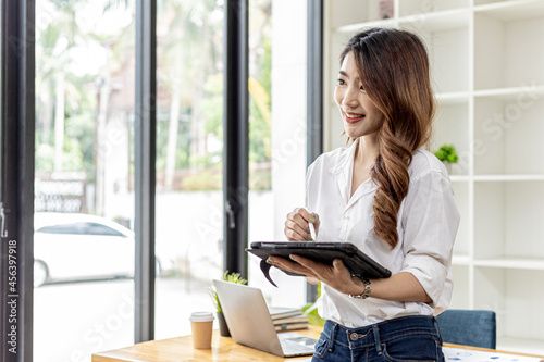 Businesswoman is using a tablet to search for information and chat, she is a business owner, she is directing employees through a tablet messenger. Asian business woman concept and use of technology.