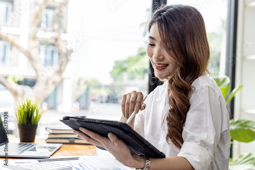 Businesswoman is using a tablet to search for information and chat, she is a business owner, she is directing employees through a tablet messenger. Asian business woman concept and use of technology.