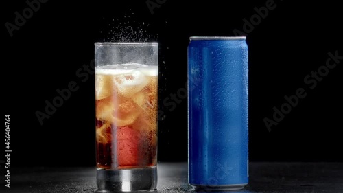 Cola with bubbles and ice cubes close-up. Cola with Ice and bubbles in glass. Chroma key can bottle. Food isolated background. Glass of Cola fizzy drink over black background b-roll. Slow motion.  photo