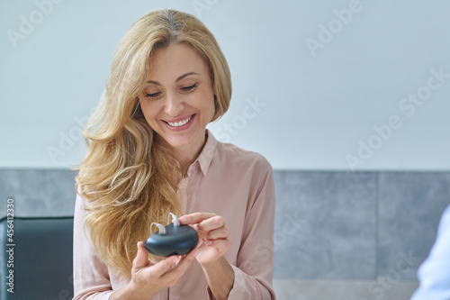 Smiling happy woman holding hearing aids in hands photo