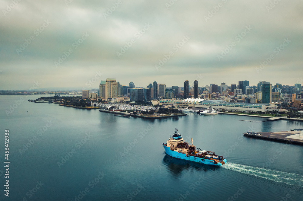 Freighter navigates San Diego bay with skyline in distance. 