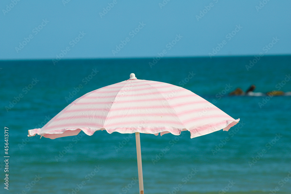 Beach umbrella with pale pink stripes in the foreground, against the blue sea background.